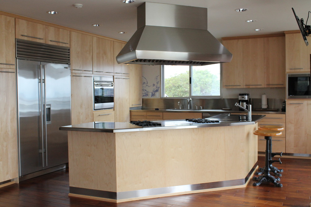 Photo of a medium sized industrial l-shaped open plan kitchen in Los Angeles with a submerged sink, flat-panel cabinets, light wood cabinets, stainless steel worktops, metallic splashback, stainless steel appliances, medium hardwood flooring and an island.