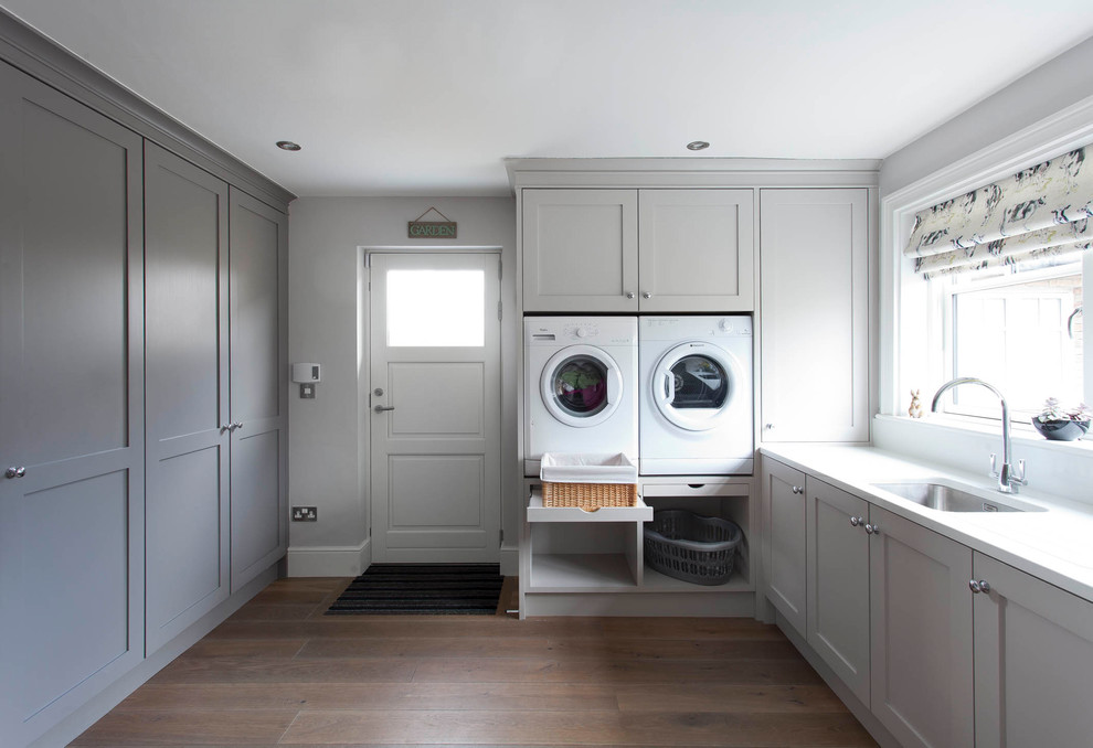 Bild på en stor vintage grå u-formad grått tvättstuga, med skåp i shakerstil, vita skåp, marmorbänkskiva, grått stänkskydd, stänkskydd i marmor, mellanmörkt trägolv och brunt golv