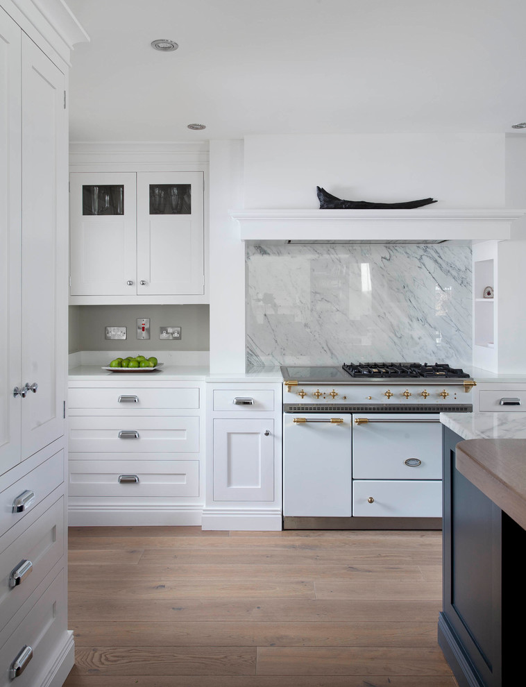 Exemple d'une grande cuisine ouverte en U avec un placard à porte shaker, des portes de placard blanches, plan de travail en marbre, une crédence grise, une crédence en marbre, un électroménager blanc, un sol en bois brun, îlot, un sol marron et un plan de travail gris.