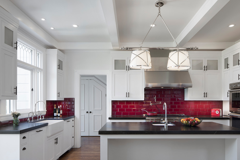 サンフランシスコにある高級な広いヴィクトリアン調のおしゃれなキッチン (エプロンフロントシンク、シェーカースタイル扉のキャビネット、白いキャビネット、クオーツストーンカウンター、赤いキッチンパネル、サブウェイタイルのキッチンパネル、シルバーの調理設備、濃色無垢フローリング、茶色い床) の写真