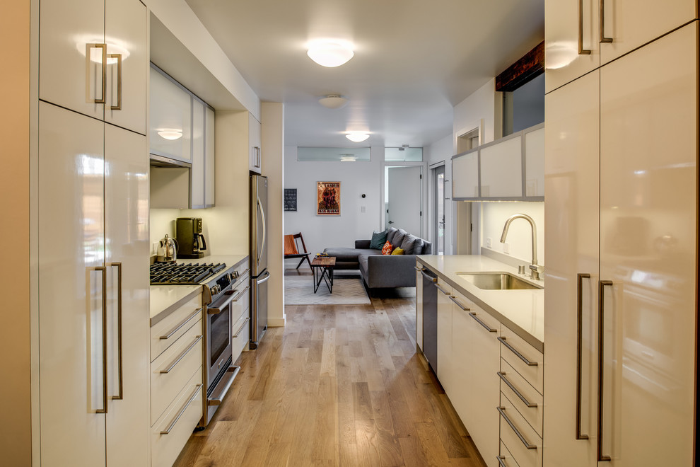 Zweizeilige Moderne Küche ohne Insel mit Unterbauwaschbecken, flächenbündigen Schrankfronten, weißen Schränken, Küchengeräten aus Edelstahl und braunem Holzboden in San Francisco