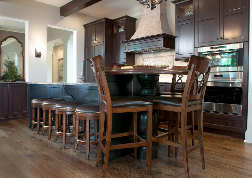 Mittelgroße Moderne Küche in L-Form mit dunklen Holzschränken, Granit-Arbeitsplatte, Küchenrückwand in Beige, Küchengeräten aus Edelstahl, braunem Holzboden und Kücheninsel in Grand Rapids