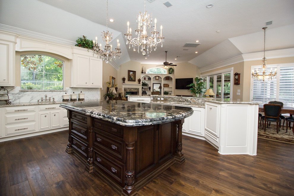 Example of a large classic u-shaped medium tone wood floor and beige floor open concept kitchen design in Houston with an undermount sink, raised-panel cabinets, white cabinets, granite countertops, white backsplash, stone slab backsplash, two islands, paneled appliances and black countertops