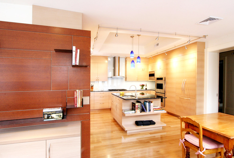 Modern inredning av ett kök och matrum, med en undermonterad diskho, släta luckor, skåp i ljust trä, vitt stänkskydd och integrerade vitvaror