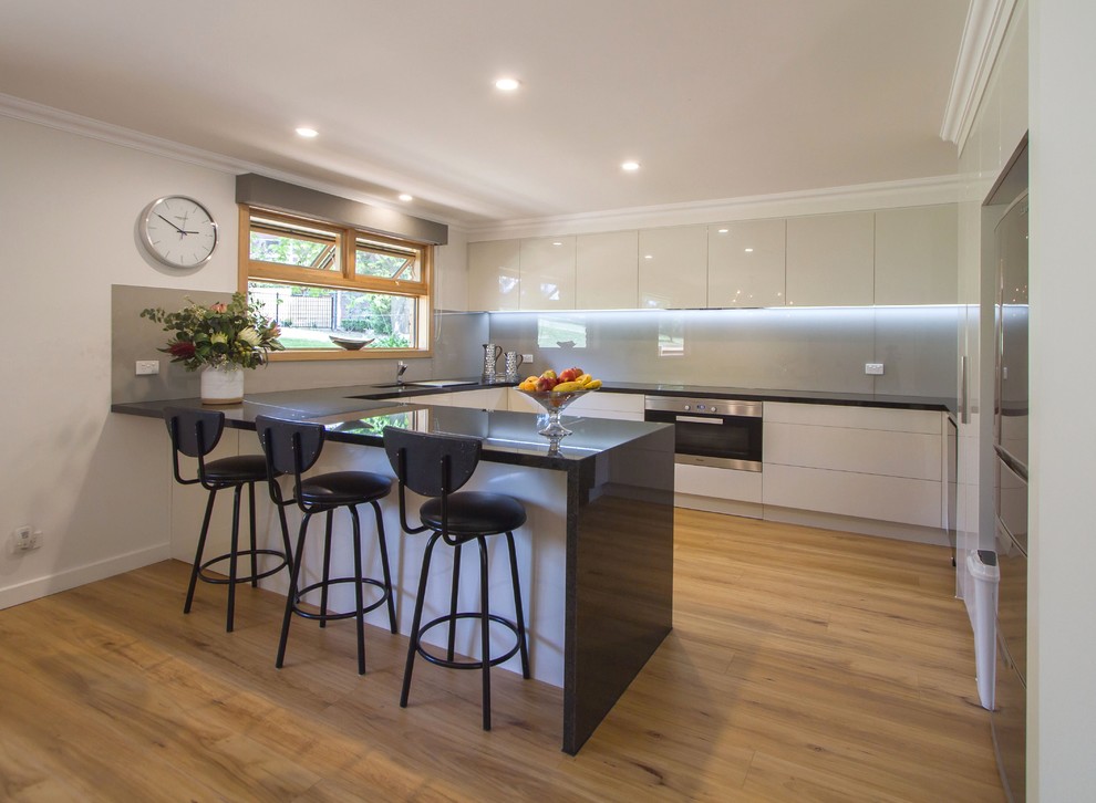 Large minimalist u-shaped light wood floor eat-in kitchen photo in Melbourne with flat-panel cabinets, granite countertops, gray backsplash, glass sheet backsplash, stainless steel appliances and a peninsula