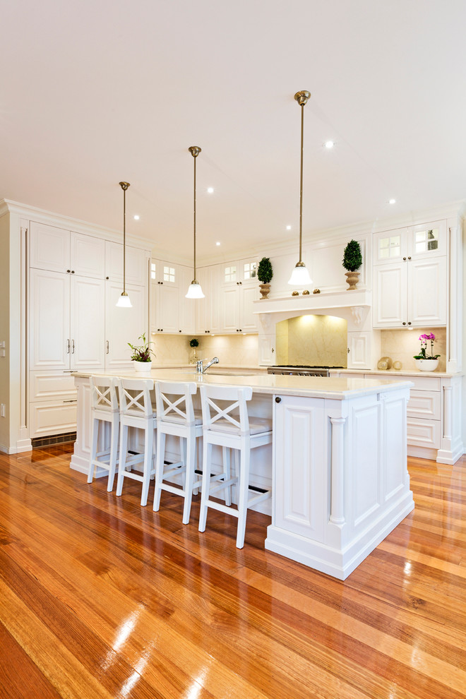 Mittelgroße Klassische Küche in L-Form mit Unterbauwaschbecken, Schrankfronten mit vertiefter Füllung, weißen Schränken, braunem Holzboden und Kücheninsel in Melbourne