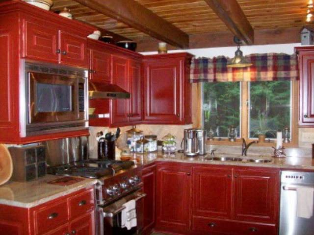 Mittelgroße Urige Wohnküche in L-Form mit Unterbauwaschbecken, profilierten Schrankfronten, roten Schränken, Granit-Arbeitsplatte, Rückwand aus Steinfliesen, bunten Elektrogeräten, braunem Holzboden und Kücheninsel in Sonstige