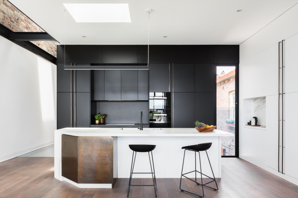 Idee per un cucina con isola centrale design con ante lisce, ante nere, paraspruzzi nero, elettrodomestici neri, pavimento in legno massello medio e top bianco