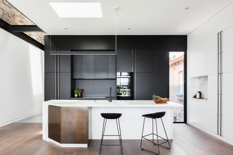 Foto di una cucina minimal con pavimento in legno massello medio, pavimento marrone, lavello integrato, ante lisce, paraspruzzi nero, elettrodomestici da incasso e top bianco