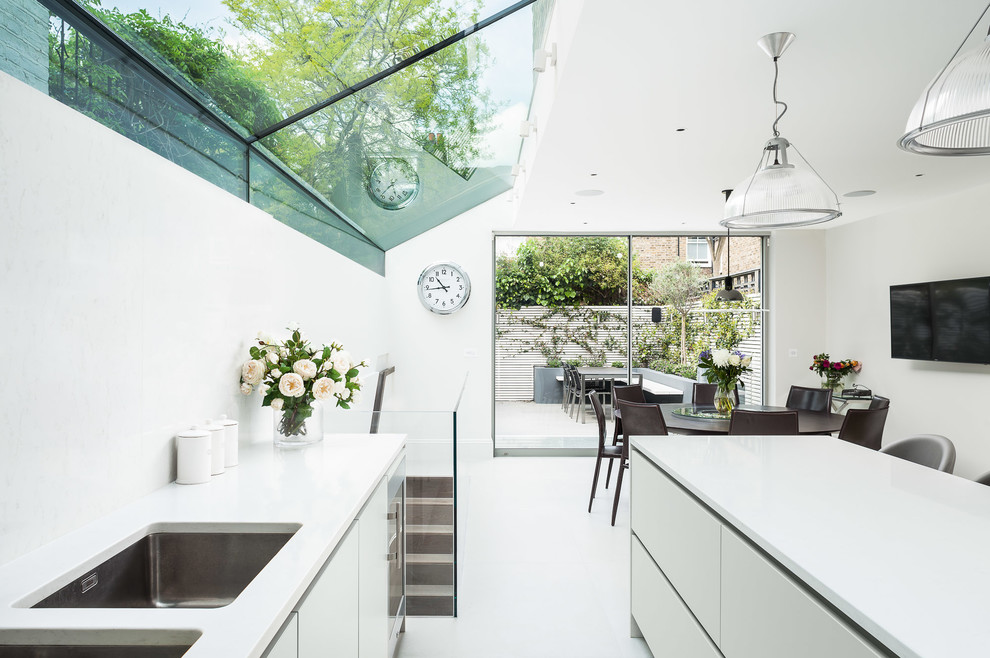Foto på ett mellanstort funkis kök, med en dubbel diskho, släta luckor, en köksö, vitt golv, vita skåp och rostfria vitvaror
