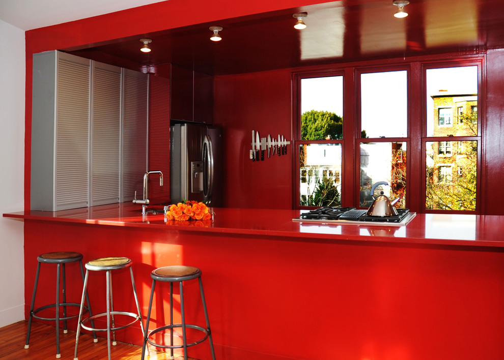 Inredning av ett modernt röd rött kök, med en undermonterad diskho, släta luckor, röda skåp, bänkskiva i koppar, rostfria vitvaror, mellanmörkt trägolv och en halv köksö