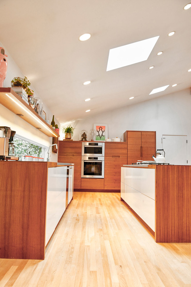 Retro inredning av ett stort vit vitt kök, med en undermonterad diskho, släta luckor, skåp i mellenmörkt trä, bänkskiva i koppar, integrerade vitvaror, ljust trägolv, en köksö och beiget golv