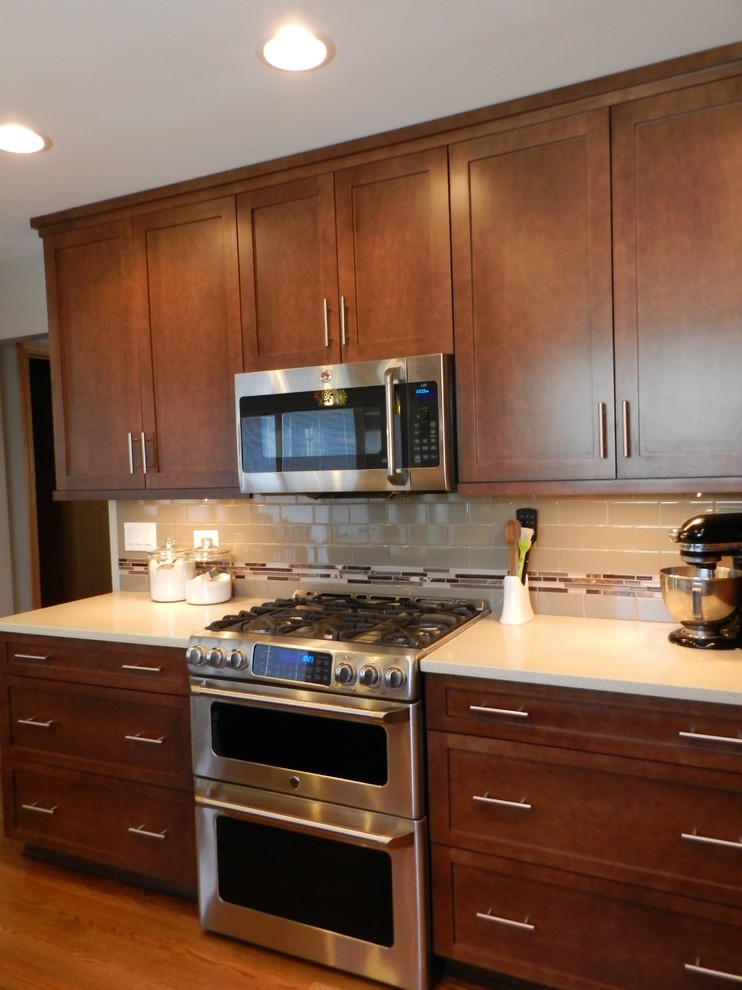 Exempel på ett mellanstort klassiskt kök, med en undermonterad diskho, skåp i shakerstil, bruna skåp, bänkskiva i kvarts, beige stänkskydd, stänkskydd i porslinskakel, rostfria vitvaror, mörkt trägolv och en halv köksö