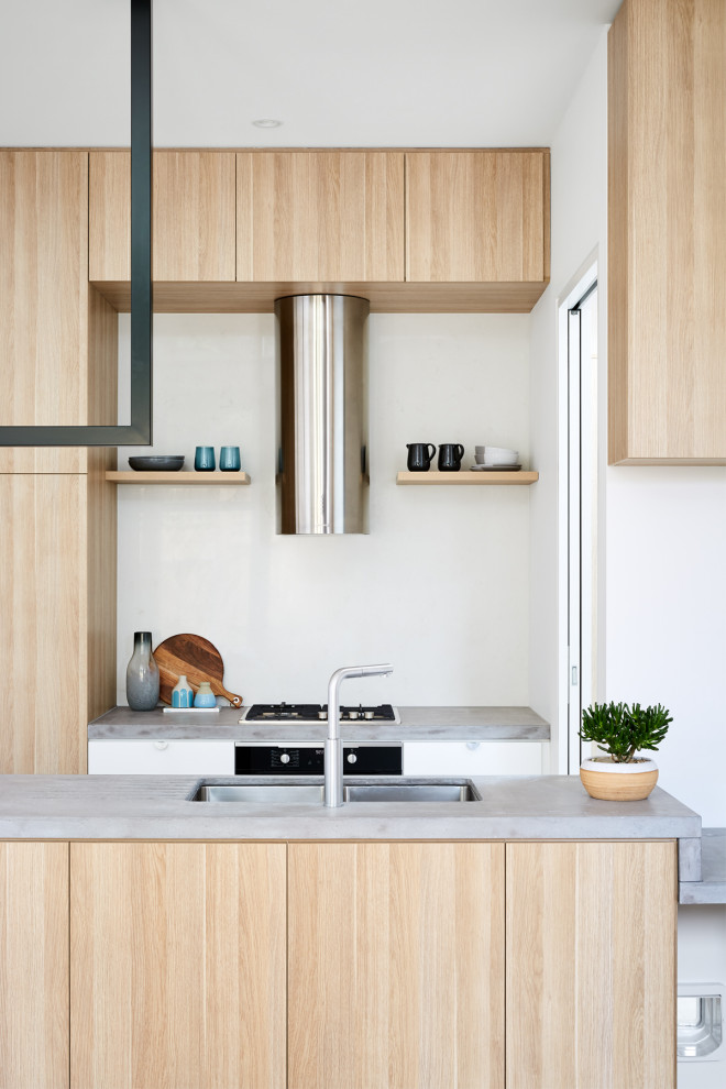 This is an example of a small contemporary u-shaped open plan kitchen in Melbourne with a built-in sink, recessed-panel cabinets, light wood cabinets, concrete worktops, white splashback, stone slab splashback, stainless steel appliances, light hardwood flooring, no island, brown floors and grey worktops.