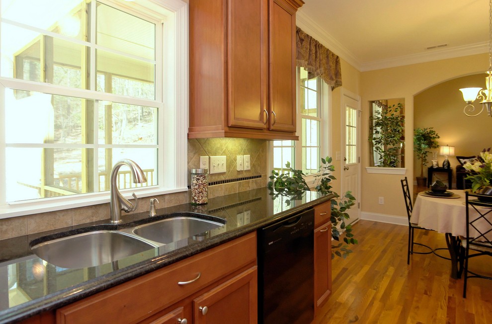 Enclosed kitchen - mid-sized traditional u-shaped light wood floor enclosed kitchen idea in Raleigh with a double-bowl sink, recessed-panel cabinets, medium tone wood cabinets, granite countertops, black backsplash, ceramic backsplash, black appliances and an island
