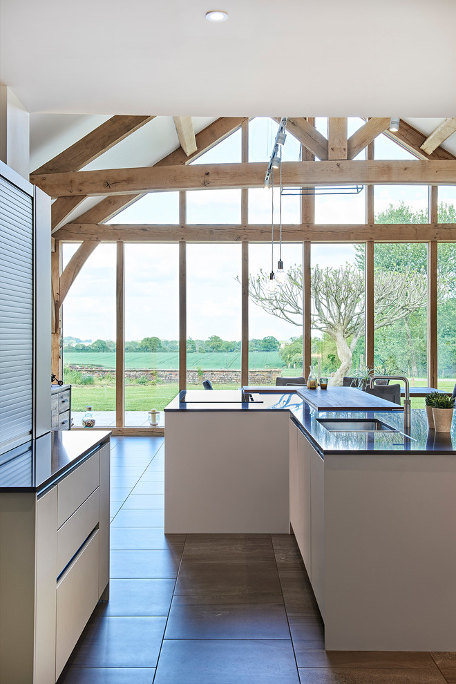 Photo of an expansive contemporary open plan kitchen in Hertfordshire with flat-panel cabinets, grey cabinets, quartz worktops, integrated appliances, porcelain flooring, multiple islands, grey floors and grey worktops.