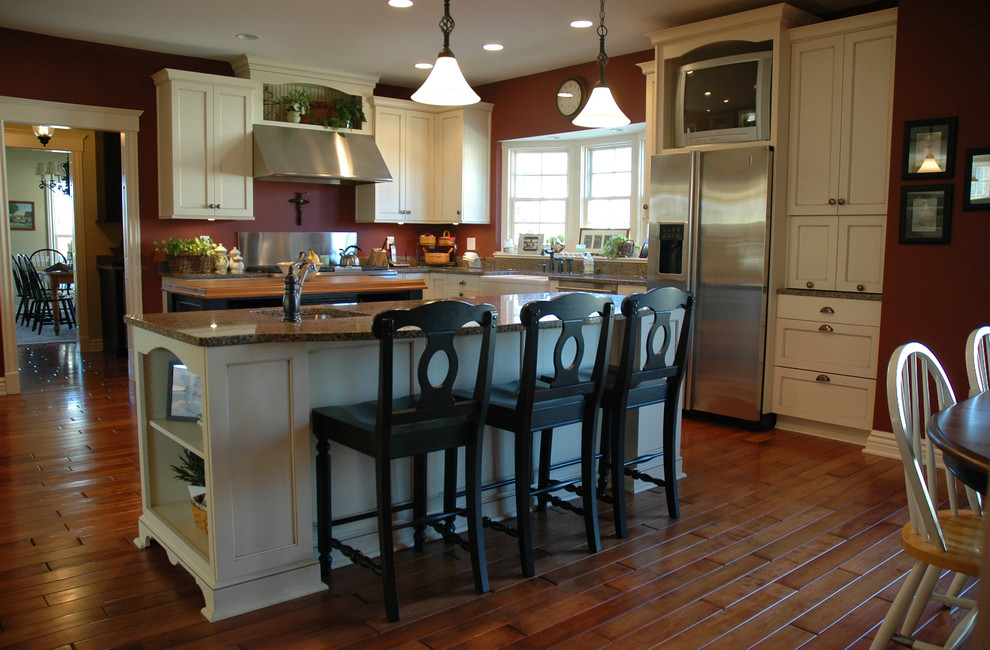 Mid-sized elegant l-shaped medium tone wood floor eat-in kitchen photo in Indianapolis with a farmhouse sink, recessed-panel cabinets, white cabinets, granite countertops, stainless steel appliances, red backsplash and an island