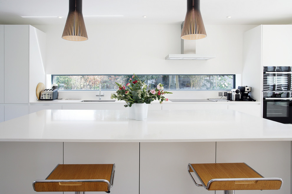 Immagine di una cucina design con lavello sottopiano, ante lisce, ante bianche, elettrodomestici neri e top bianco