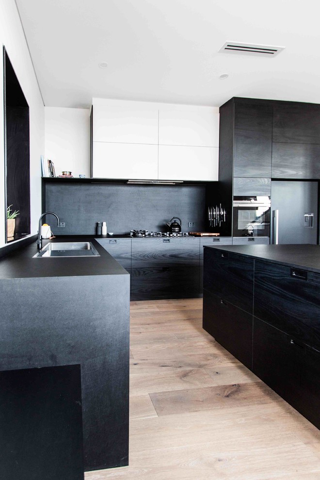 Idéer för ett stort modernt kök, med en nedsänkt diskho, släta luckor, svarta skåp, svart stänkskydd, svarta vitvaror, ljust trägolv och en köksö