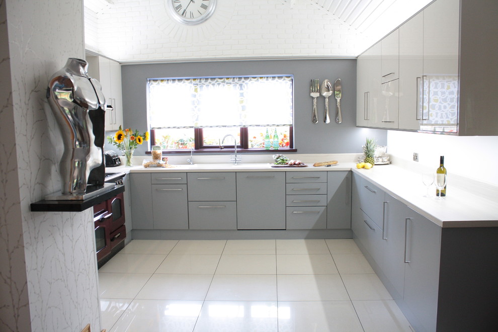 На фото: п-образная кухня-гостиная среднего размера в стиле модернизм с одинарной мойкой, плоскими фасадами, серыми фасадами, столешницей из ламината, серым фартуком, фартуком из стекла и полом из керамогранита с