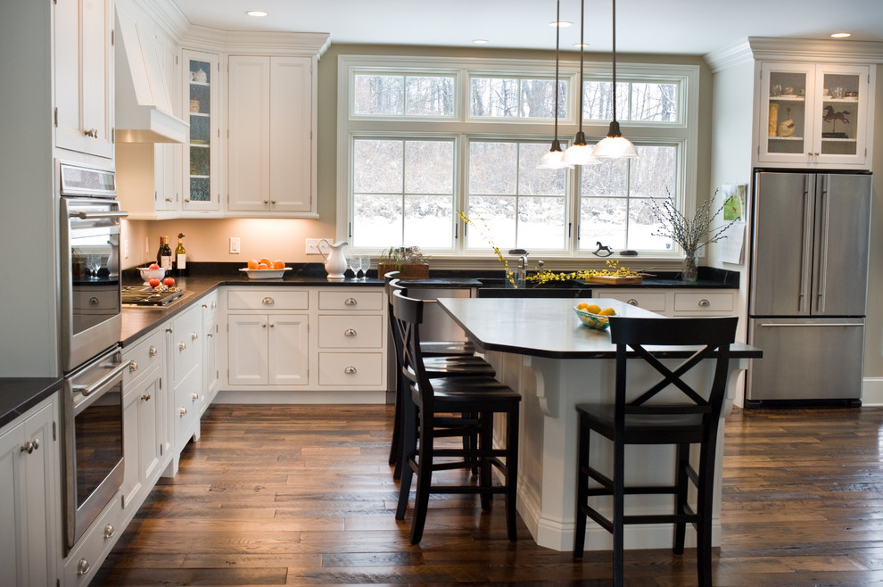 Inspiration for a traditional l-shaped kitchen/diner in Boston with a belfast sink, flat-panel cabinets, stainless steel cabinets, soapstone worktops, stainless steel appliances, medium hardwood flooring and an island.