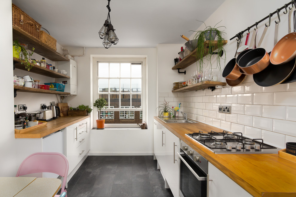 Inspiration for a contemporary galley kitchen in Surrey with a built-in sink, flat-panel cabinets, white cabinets, wood worktops, white splashback, metro tiled splashback, grey floors, brown worktops and no island.