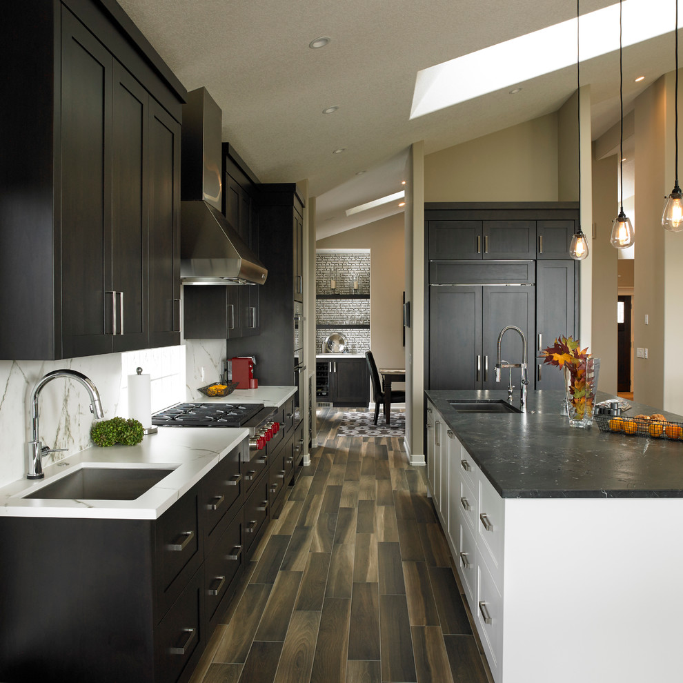 Minimalist l-shaped porcelain tile open concept kitchen photo in Calgary with an undermount sink, shaker cabinets, dark wood cabinets, granite countertops, white backsplash, stone slab backsplash, stainless steel appliances and an island