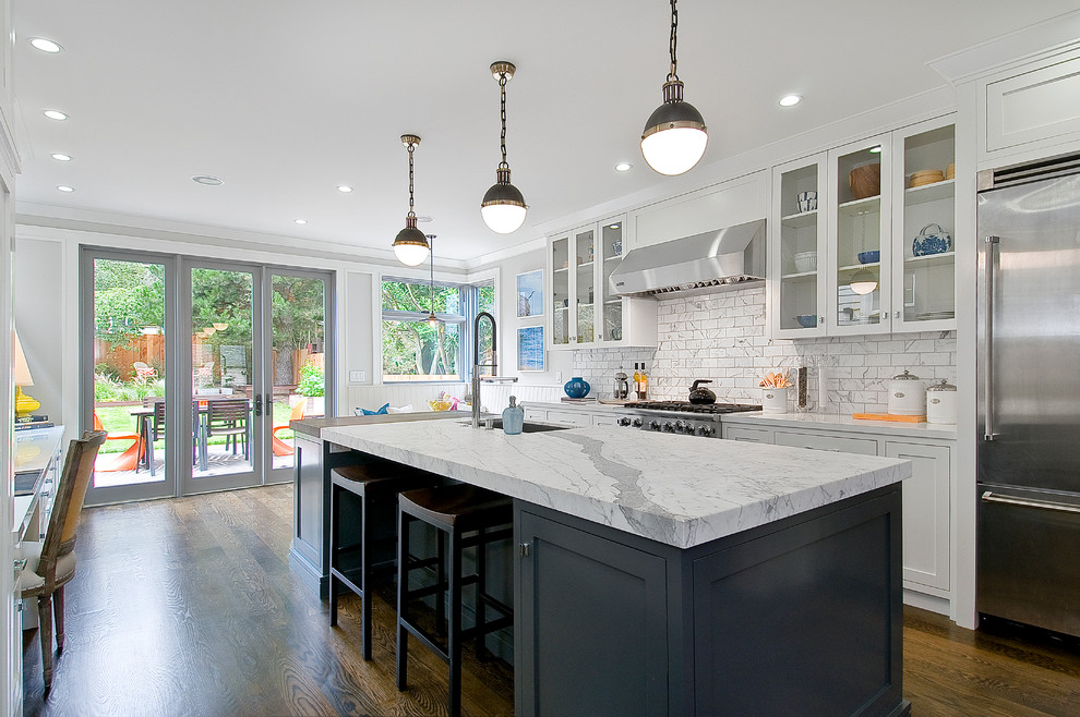 Example of a transitional dark wood floor kitchen design in San Francisco with an undermount sink, glass-front cabinets, white cabinets, marble countertops, multicolored backsplash, subway tile backsplash, stainless steel appliances and an island