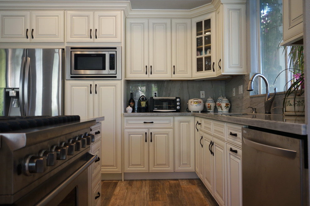 Klassische Küche in L-Form mit profilierten Schrankfronten, weißen Schränken, Quarzit-Arbeitsplatte, Rückwand aus Stein, Küchengeräten aus Edelstahl und Kücheninsel in Orange County