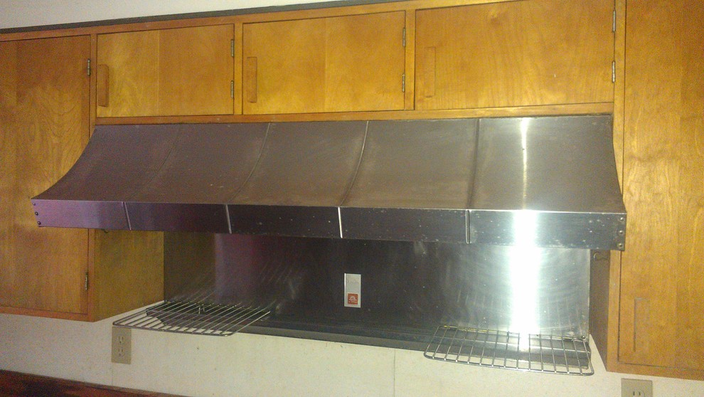 ボストンにある低価格の中くらいなミッドセンチュリースタイルのおしゃれなキッチン (ドロップインシンク、フラットパネル扉のキャビネット、淡色木目調キャビネット、木材カウンター、黒い調理設備) の写真