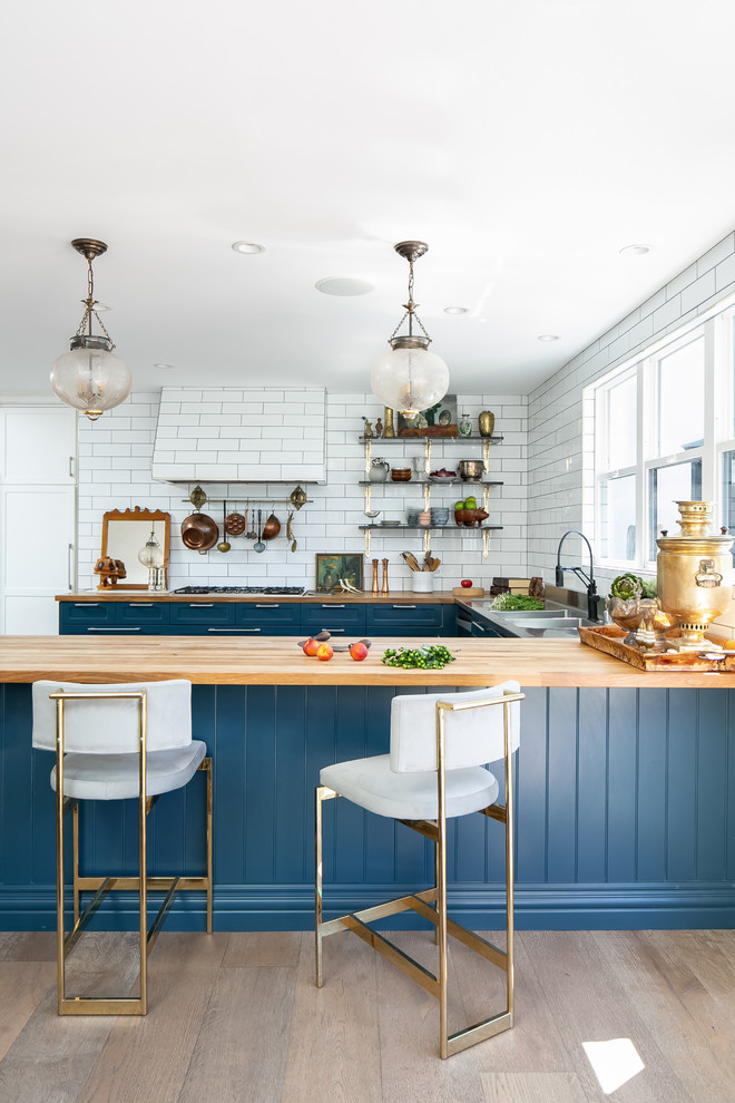Photo of a nautical u-shaped kitchen in Orange County with blue cabinets, wood worktops, white splashback, metro tiled splashback, light hardwood flooring and a breakfast bar.