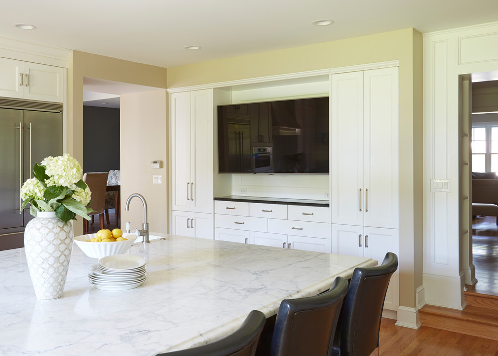 Inredning av ett klassiskt avskilt, mycket stort u-kök, med en undermonterad diskho, skåp i shakerstil, vita skåp, marmorbänkskiva, vitt stänkskydd, stänkskydd i sten, rostfria vitvaror, mellanmörkt trägolv och en köksö