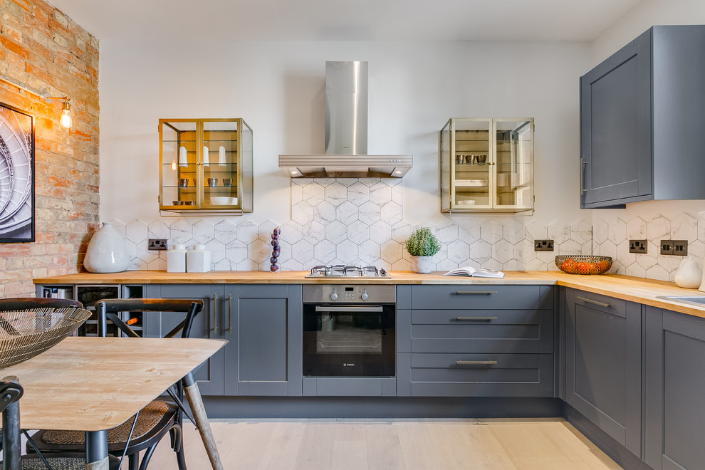 Traditional l-shaped kitchen/diner in London with a built-in sink, shaker cabinets, grey cabinets, wood worktops, white splashback, stainless steel appliances, light hardwood flooring, no island, beige floors and brown worktops.