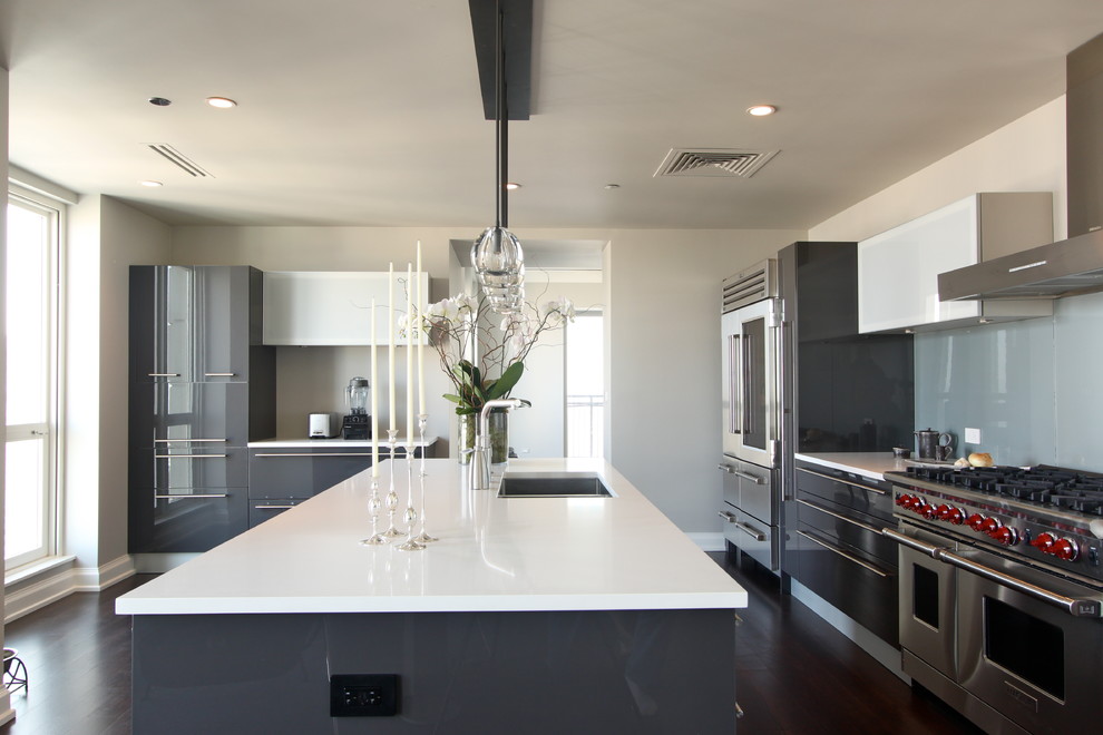 Example of a large minimalist l-shaped dark wood floor enclosed kitchen design in Boston with an undermount sink, flat-panel cabinets, gray cabinets, solid surface countertops, gray backsplash, glass sheet backsplash, stainless steel appliances and an island
