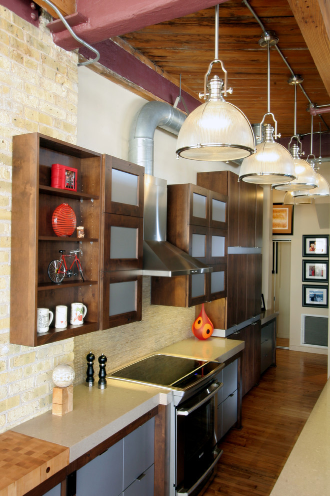 Inspiration for a small industrial galley medium tone wood floor eat-in kitchen remodel in Milwaukee with an undermount sink, flat-panel cabinets, dark wood cabinets, quartz countertops, beige backsplash, stone tile backsplash, stainless steel appliances and a peninsula