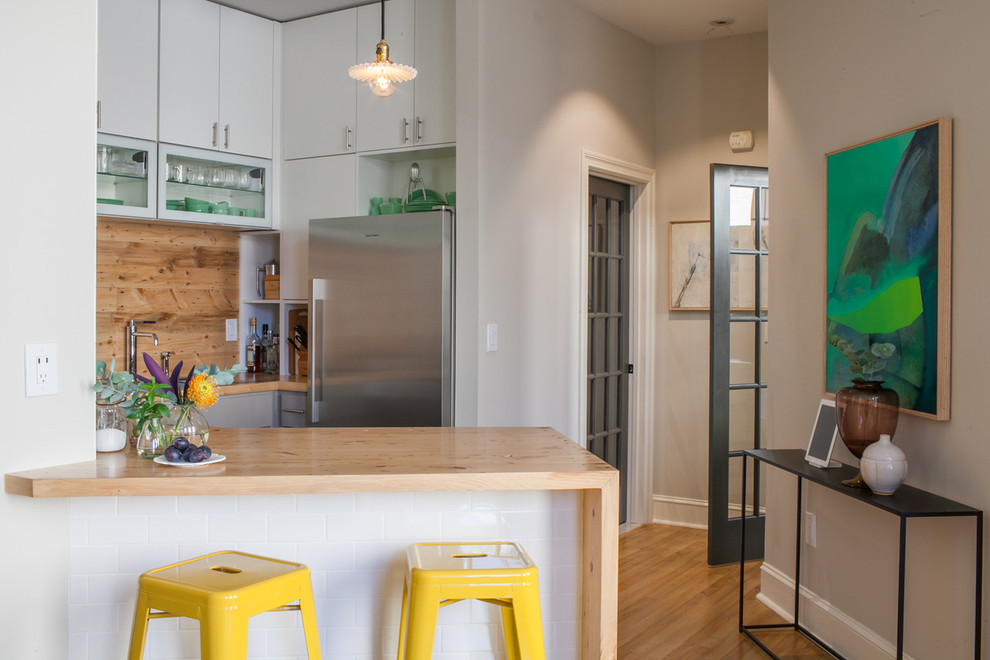 Cette image montre une cuisine design avec un placard à porte plane, des portes de placard blanches, un plan de travail en bois et un électroménager en acier inoxydable.