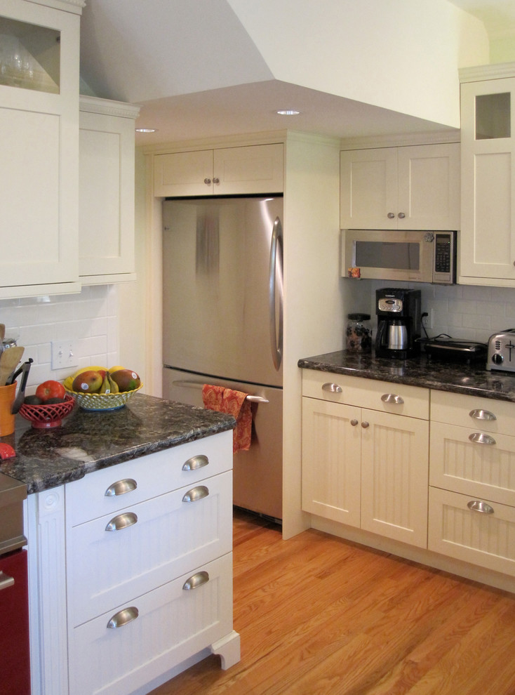 Example of a small cottage u-shaped light wood floor enclosed kitchen design in San Luis Obispo with an undermount sink, shaker cabinets, white cabinets, granite countertops, white backsplash, ceramic backsplash, white appliances and a peninsula