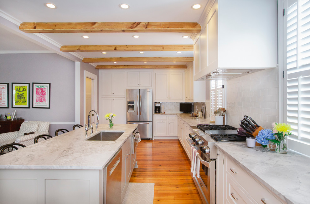 Klassische Küche in U-Form mit Unterbauwaschbecken, Küchenrückwand in Weiß, Rückwand aus Metrofliesen, Küchengeräten aus Edelstahl, Kücheninsel und braunem Holzboden in Charleston