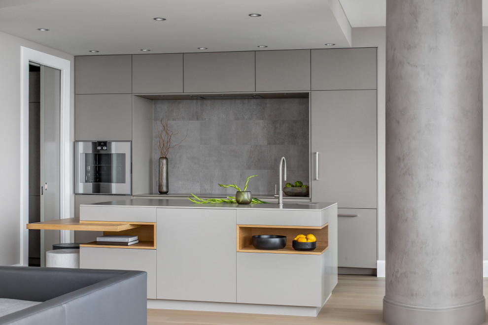Foto på ett funkis grå kök och matrum, med en undermonterad diskho, släta luckor, grå skåp, bänkskiva i kvarts, grått stänkskydd, integrerade vitvaror, mellanmörkt trägolv, en köksö och brunt golv