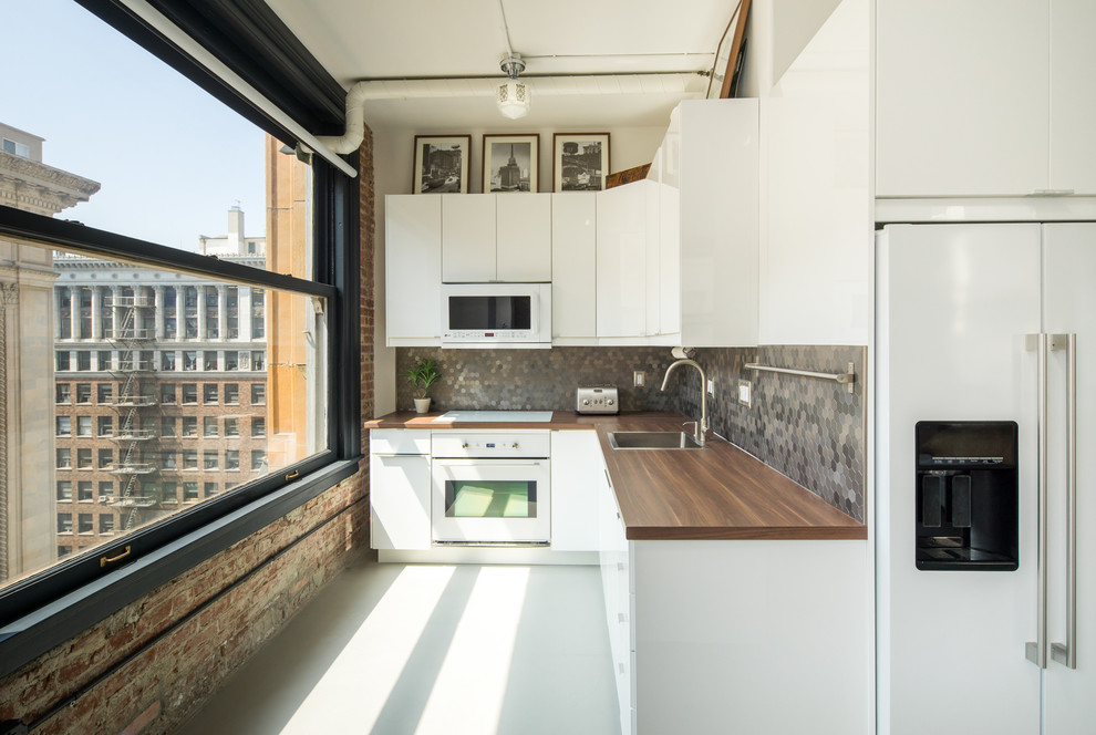 Photo of an urban l-shaped kitchen in Los Angeles with a built-in sink, flat-panel cabinets, white cabinets, wood worktops, grey splashback, mosaic tiled splashback and white appliances.