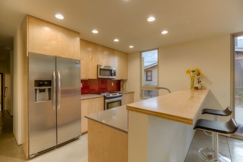 Example of a small 1960s galley concrete floor kitchen design in Albuquerque with a double-bowl sink, flat-panel cabinets, light wood cabinets, quartzite countertops, red backsplash, glass sheet backsplash and stainless steel appliances