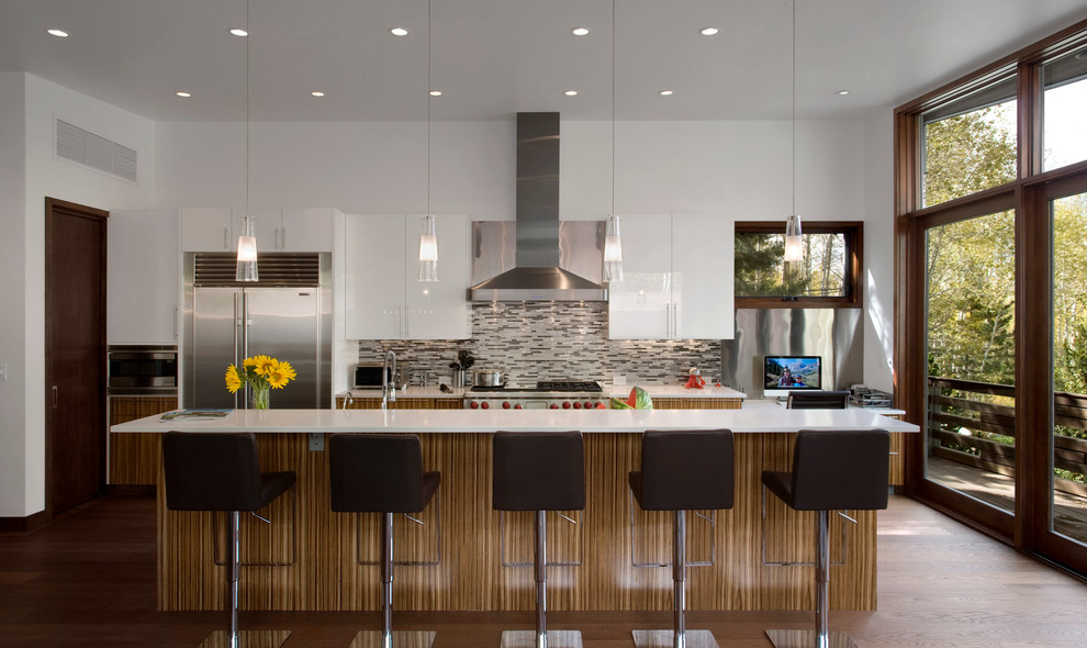 Example of a mid-sized trendy galley medium tone wood floor eat-in kitchen design in Denver with flat-panel cabinets, white cabinets, quartz countertops, stainless steel appliances, an island and gray backsplash