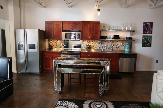 Small urban single-wall concrete floor and brown floor open concept kitchen photo in Other with a single-bowl sink, shaker cabinets, medium tone wood cabinets, stainless steel countertops, multicolored backsplash, glass tile backsplash, stainless steel appliances, an island and gray countertops