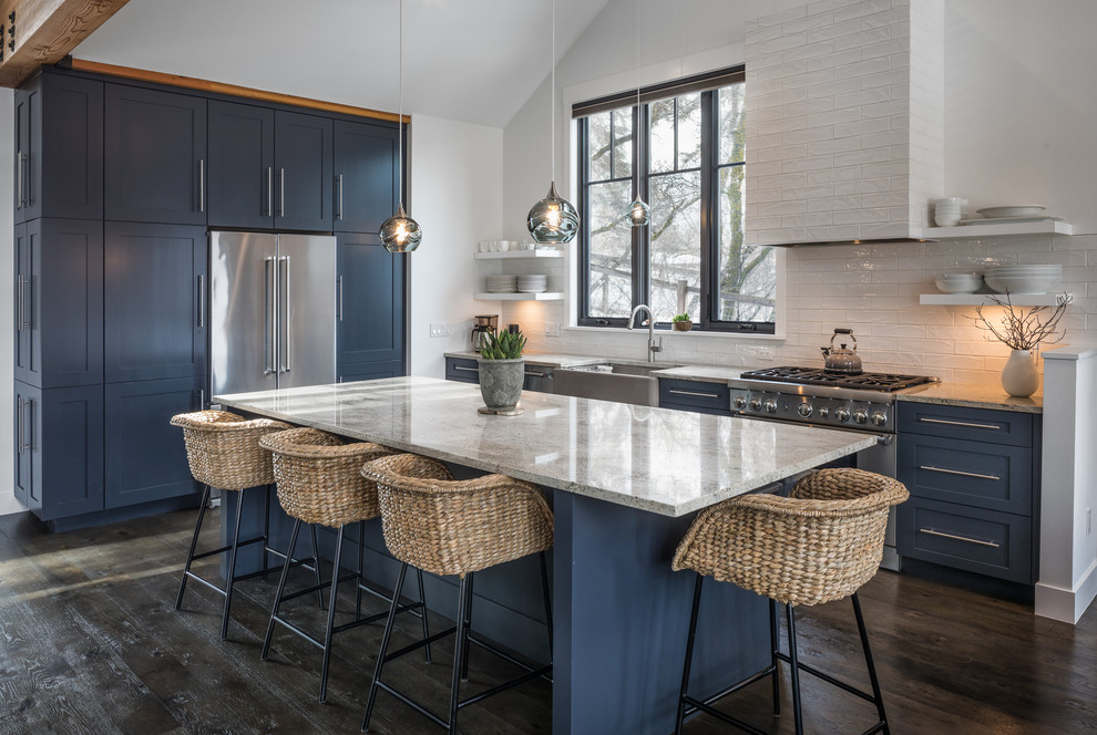 Urige Küche mit Landhausspüle, Schrankfronten im Shaker-Stil, blauen Schränken, Küchenrückwand in Weiß, Küchengeräten aus Edelstahl, dunklem Holzboden und Kücheninsel in Sonstige