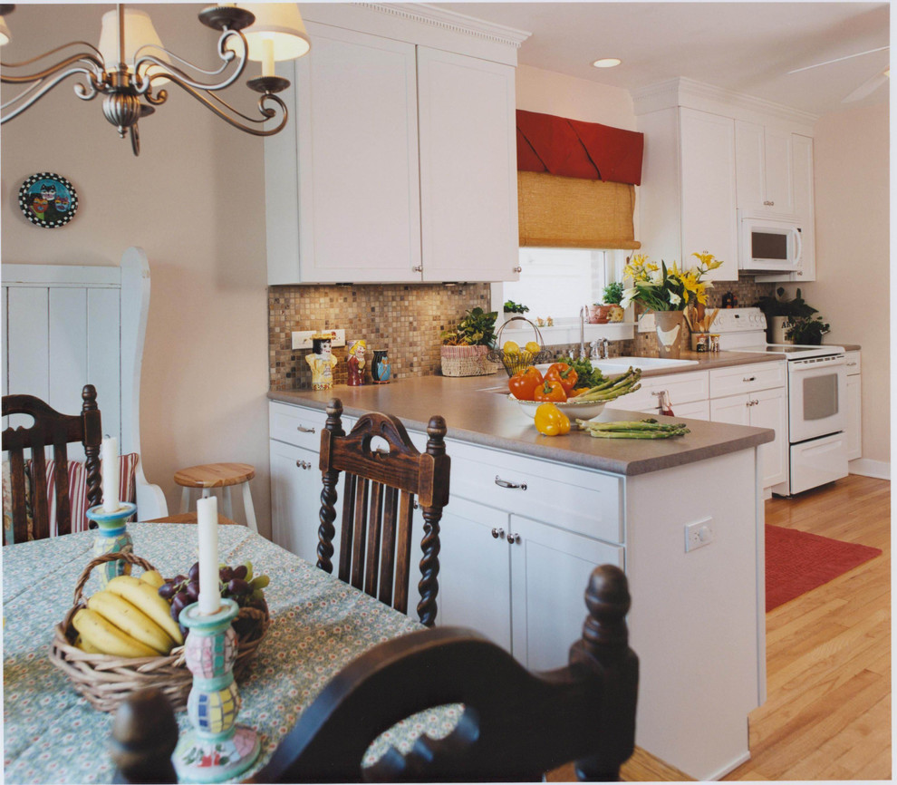 This is an example of a medium sized traditional l-shaped kitchen/diner in Chicago with a built-in sink, beaded cabinets, white cabinets, laminate countertops, brown splashback, white appliances and light hardwood flooring.