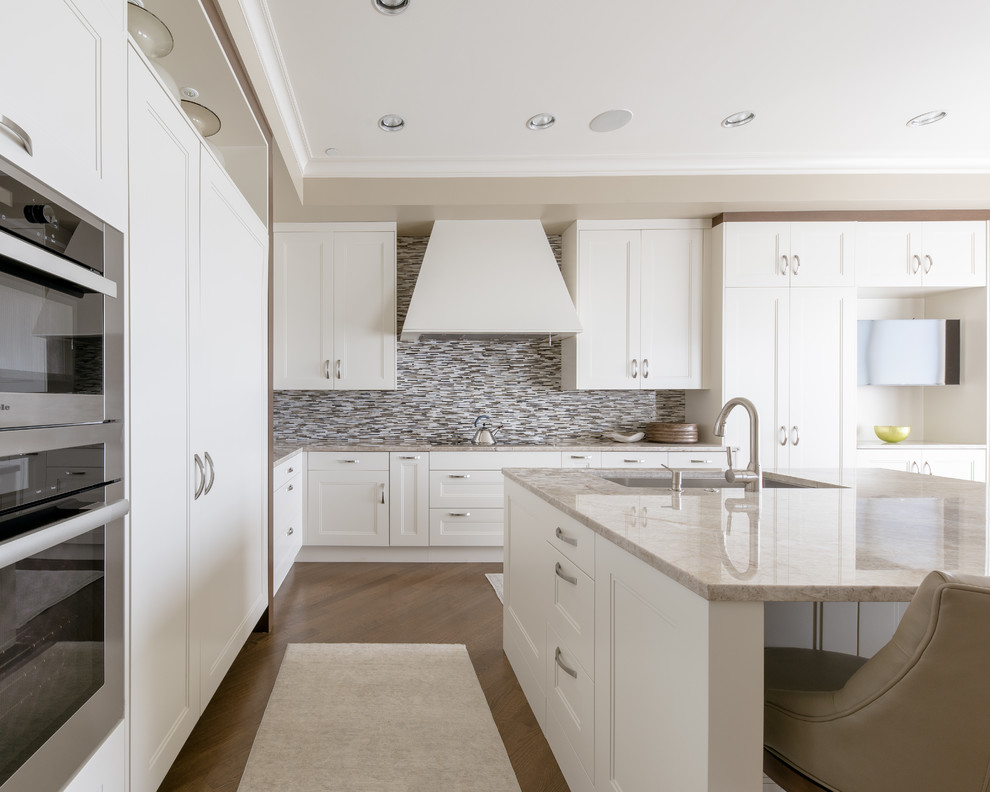 Eat-in kitchen - large transitional u-shaped light wood floor and brown floor eat-in kitchen idea in Dallas with an undermount sink, shaker cabinets, white cabinets, quartzite countertops, beige backsplash, glass tile backsplash, stainless steel appliances and an island