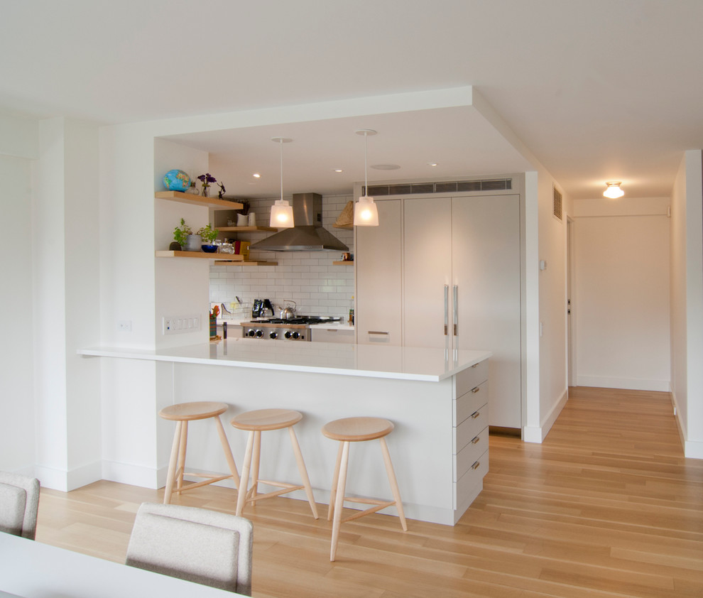 Example of a mid-sized trendy galley light wood floor and beige floor eat-in kitchen design in New York with an undermount sink, flat-panel cabinets, gray cabinets, glass countertops, white backsplash, subway tile backsplash, paneled appliances and an island