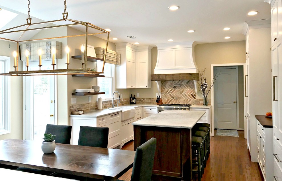 Inspiration for a mid-sized farmhouse l-shaped medium tone wood floor and brown floor eat-in kitchen remodel in Philadelphia with a farmhouse sink, shaker cabinets, white cabinets, granite countertops, red backsplash, brick backsplash, paneled appliances, an island and gray countertops