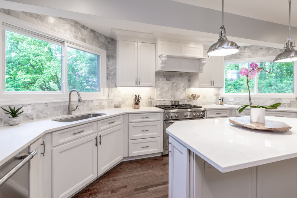Modern inredning av ett mellanstort vit vitt kök och matrum, med vita skåp, granitbänkskiva, grått stänkskydd, rostfria vitvaror, en köksö och brunt golv
