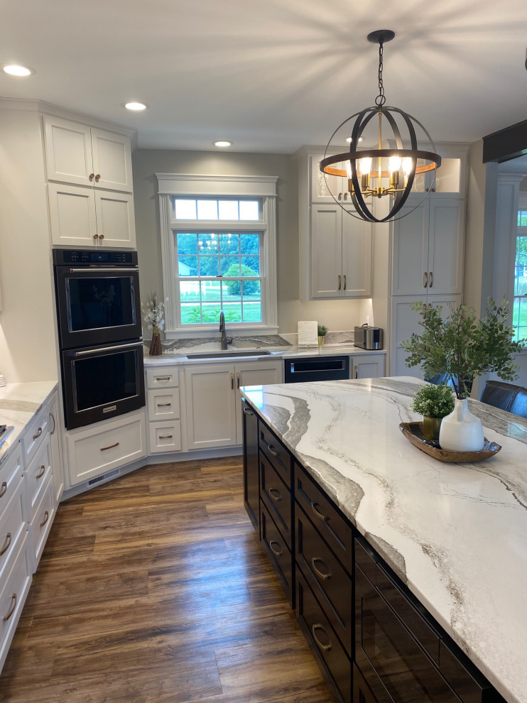 Inspiration for a large transitional l-shaped medium tone wood floor and brown floor open concept kitchen remodel in Other with an undermount sink, flat-panel cabinets, white cabinets, quartz countertops, multicolored backsplash, quartz backsplash, black appliances, an island and multicolored countertops